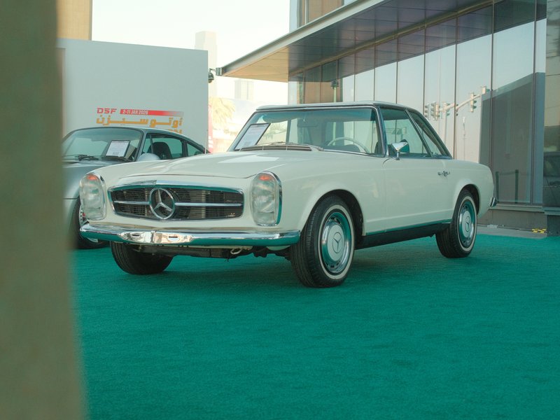 Classic white Mercedes-Benz car parked on green carpet in a modern setting.