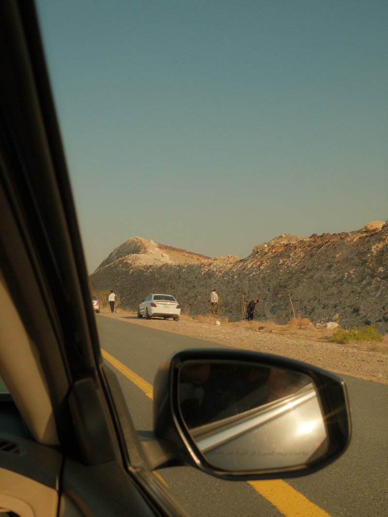 View from a car window showing a road alongside a rocky landscape with a distant white car.