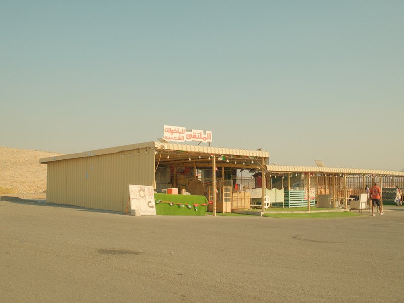 A small roadside shop with colorful wooden structures under a clear sky, surrounded by arid landscape.