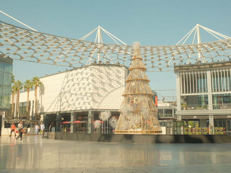 A large Christmas tree in a modern urban plaza with a patterned canopy overhead.