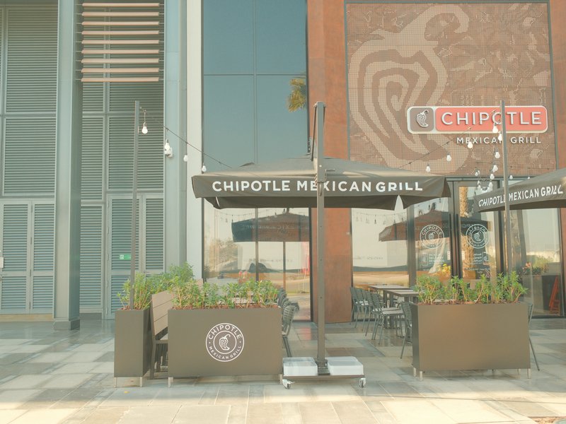 Exterior view of a Chipotle restaurant with outdoor seating and umbrellas.