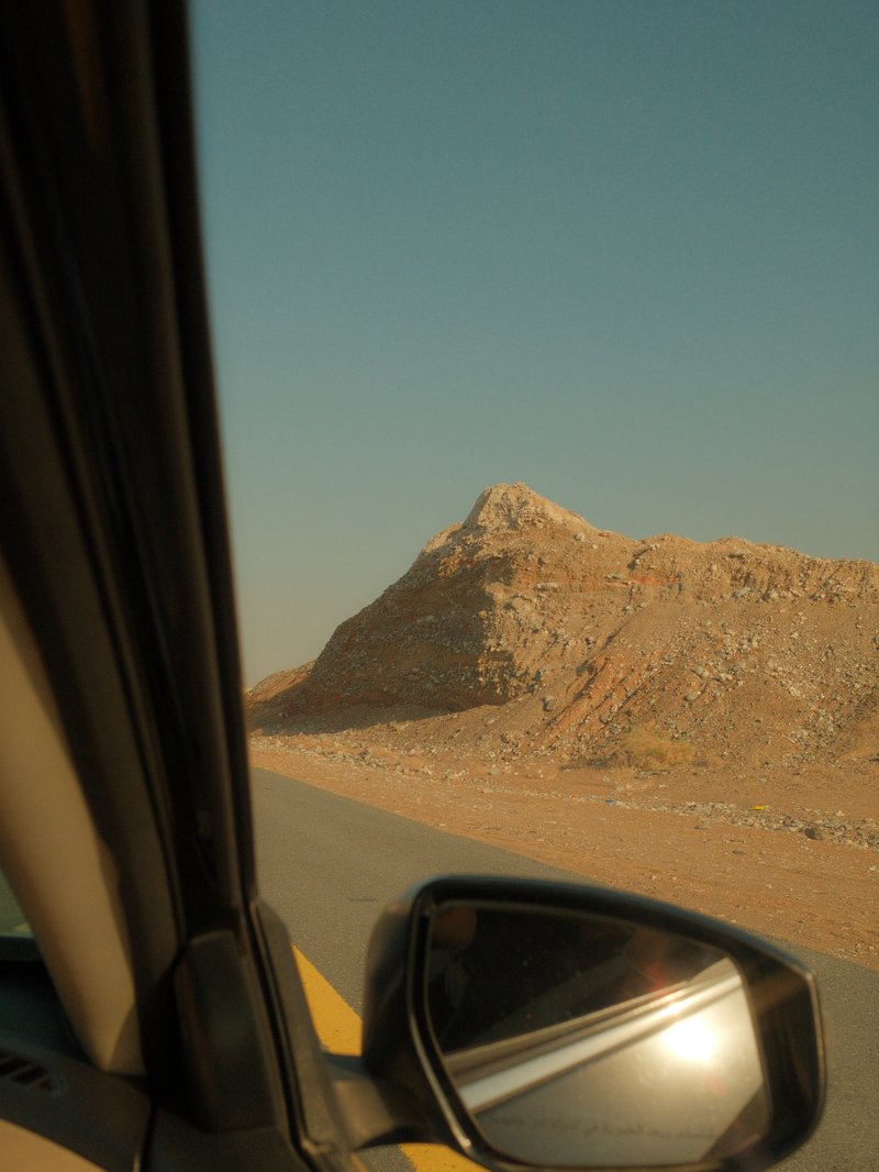 View from a car window showing a rocky hill and a clear blue sky.