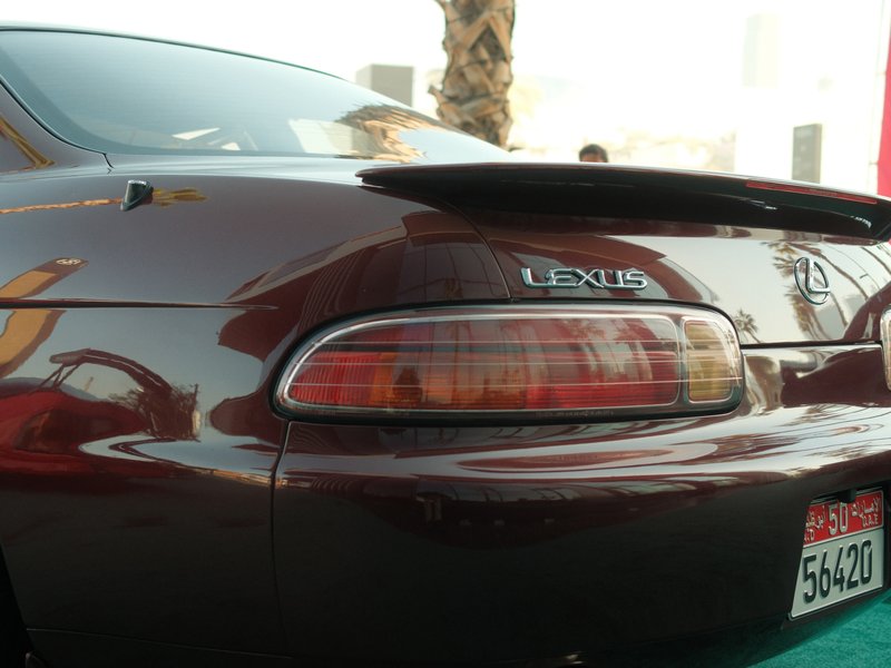 Close-up of the rear of a dark-colored Lexus car with a distinctive spoiler and taillights.