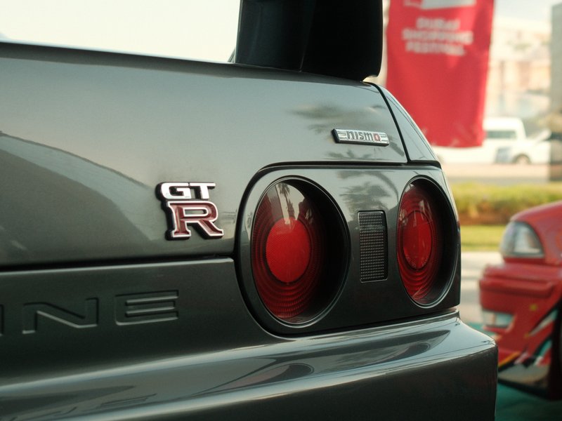 Close-up of a gray sports car's rear with GT-R badge and round taillights, blurred background.