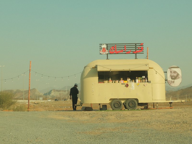 A person walking towards a vintage food trailer in a desert landscape under a clear sky.