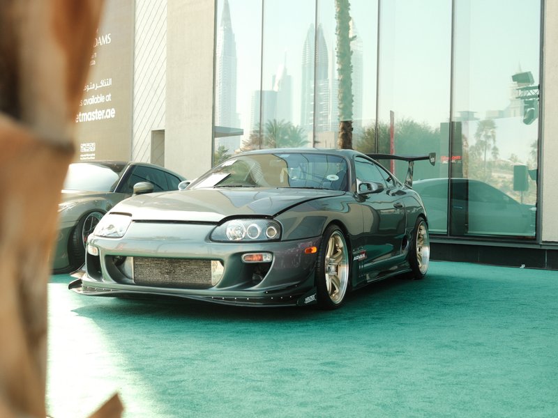 A modified black sports car parked on green carpet outside a building with glass windows.