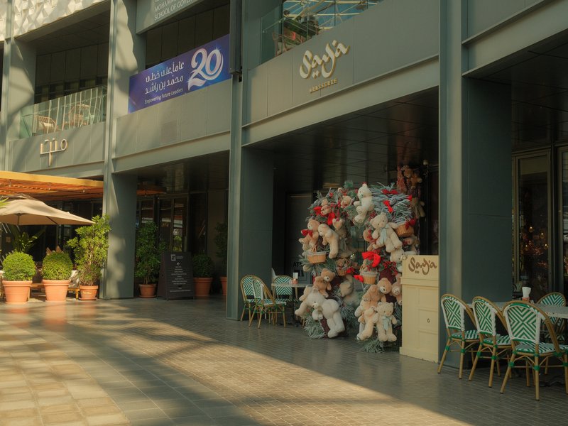 Two people in traditional costumes sitting outside a café with colorful decorations and plants.