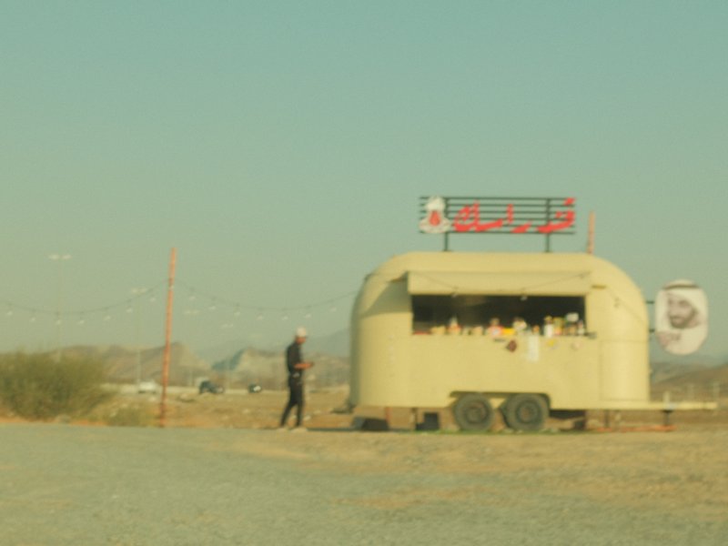 A vintage food trailer in a barren landscape with a person standing nearby under a clear sky.