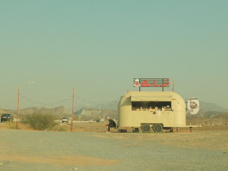 A vintage roadside diner in a desert landscape with mountains in the background under a clear sky.