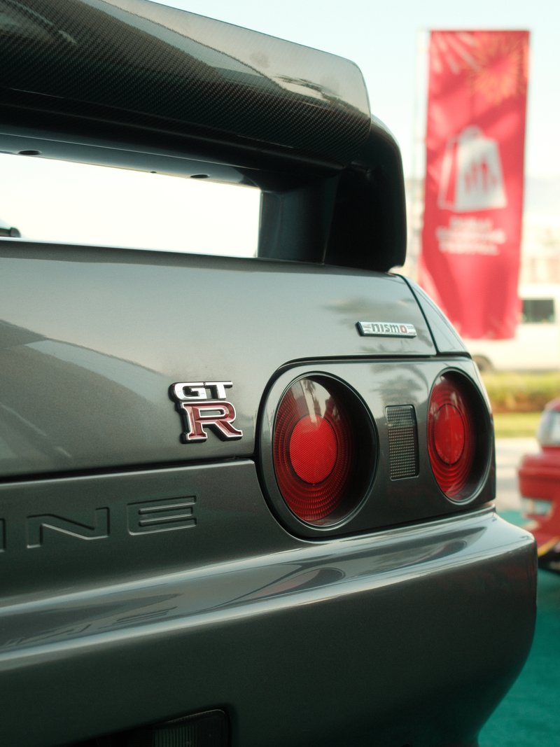 Close-up of a gray sports car's rear with GT-R badge and red taillights, blurred background.