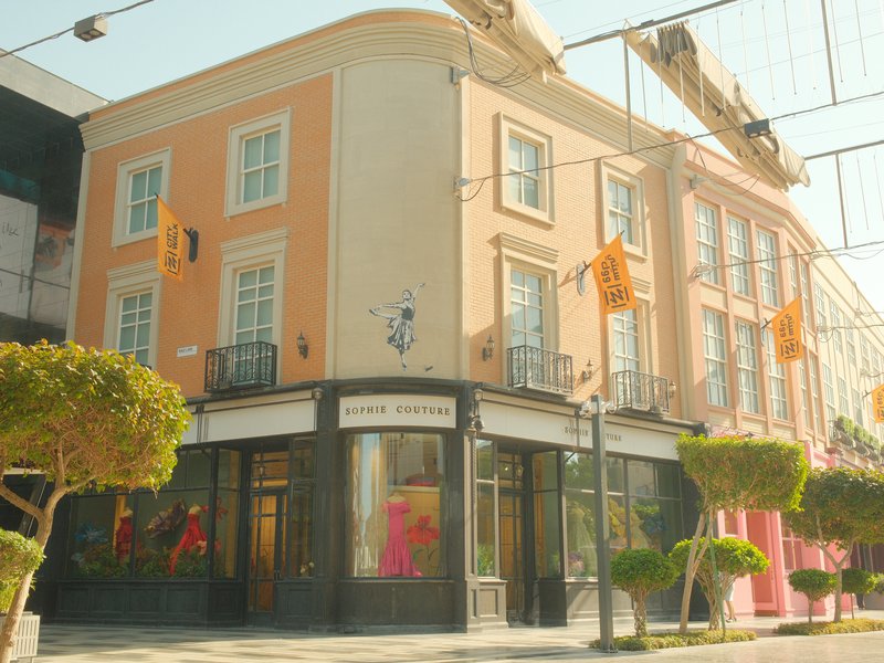 A pastel-colored building with large windows and decorative plants in an urban setting.