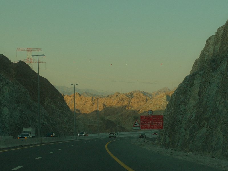 A winding road through rocky mountains at dusk with a hint of sunset colors in the background.