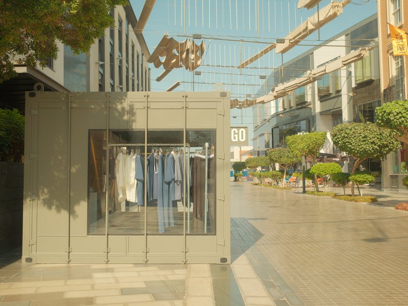 A modern clothing store display in a sunny urban shopping area with greenery and pedestrian walkways.