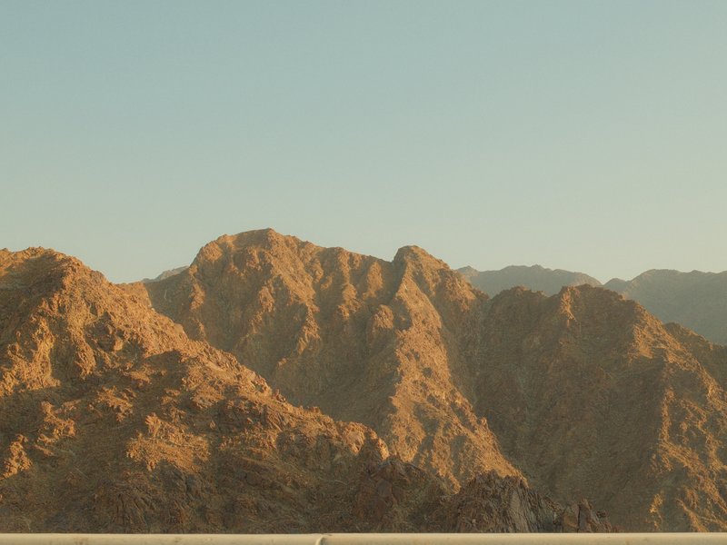 A scenic view of rugged mountains under a clear sky, showcasing warm tones of the landscape.