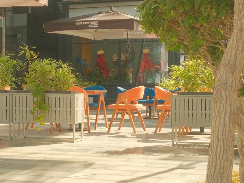 Outdoor café scene with colorful chairs and plants under umbrellas.