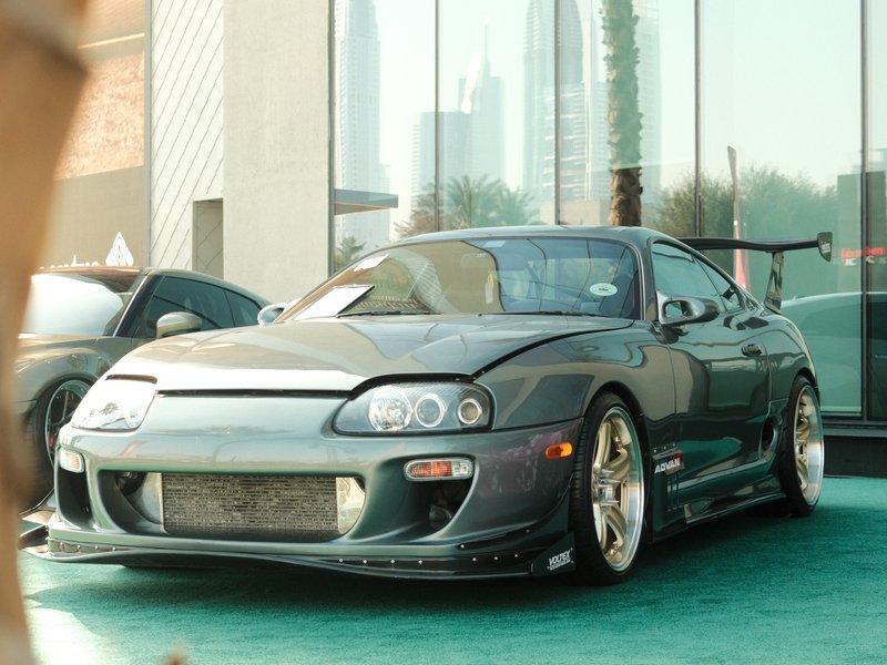 A modified gray sports car parked in front of a glass building, showcasing its sleek design and custom features.