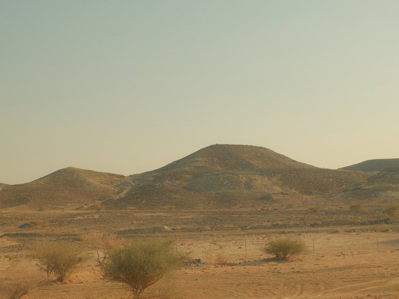 A distant view of rolling hills in a desert landscape under a hazy sky.