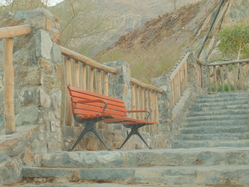 A red bench beside stone steps and a wooden railing in a natural setting.