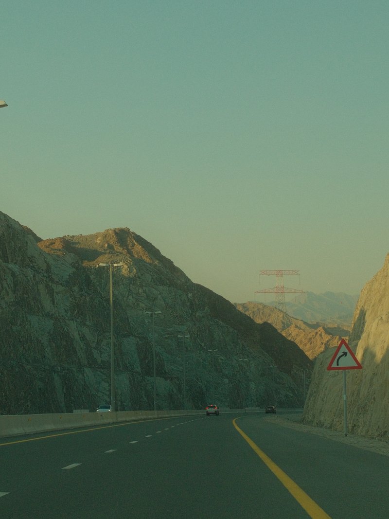 A winding road through rocky mountains under a pale sky during golden hour.