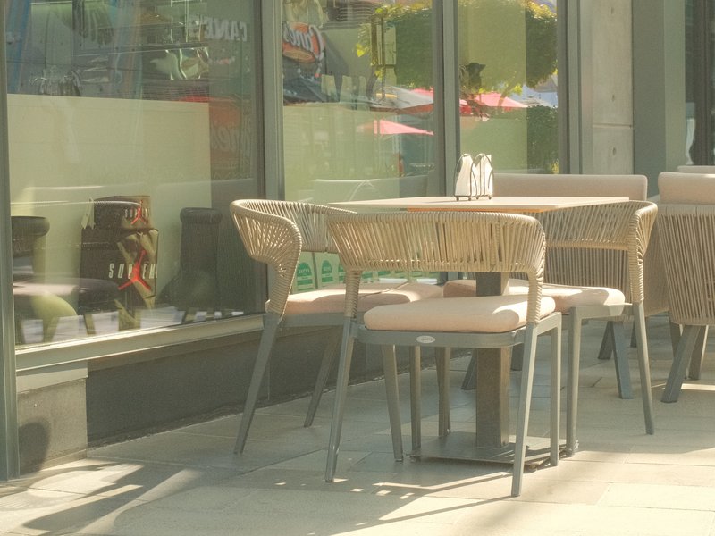 A cozy outdoor café setting with empty chairs and tables under soft sunlight.