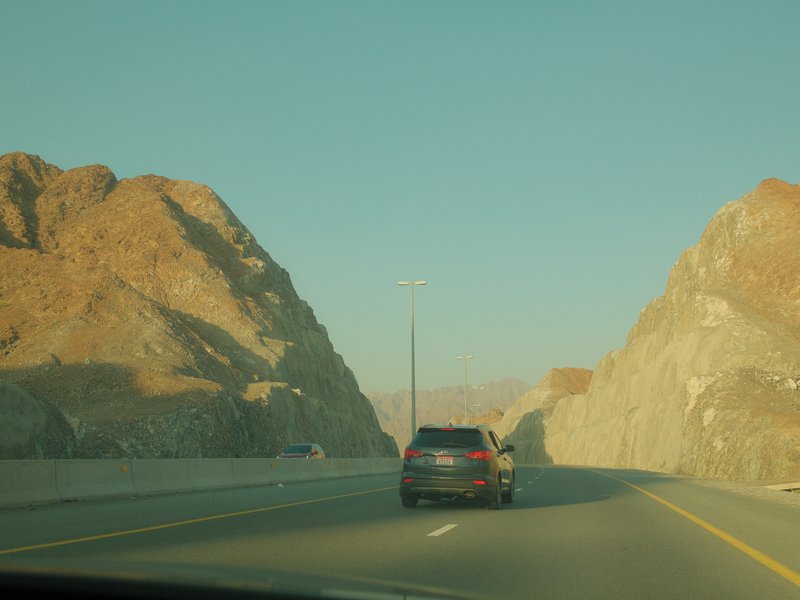 A car driving on a highway surrounded by rocky mountains under a clear sky.