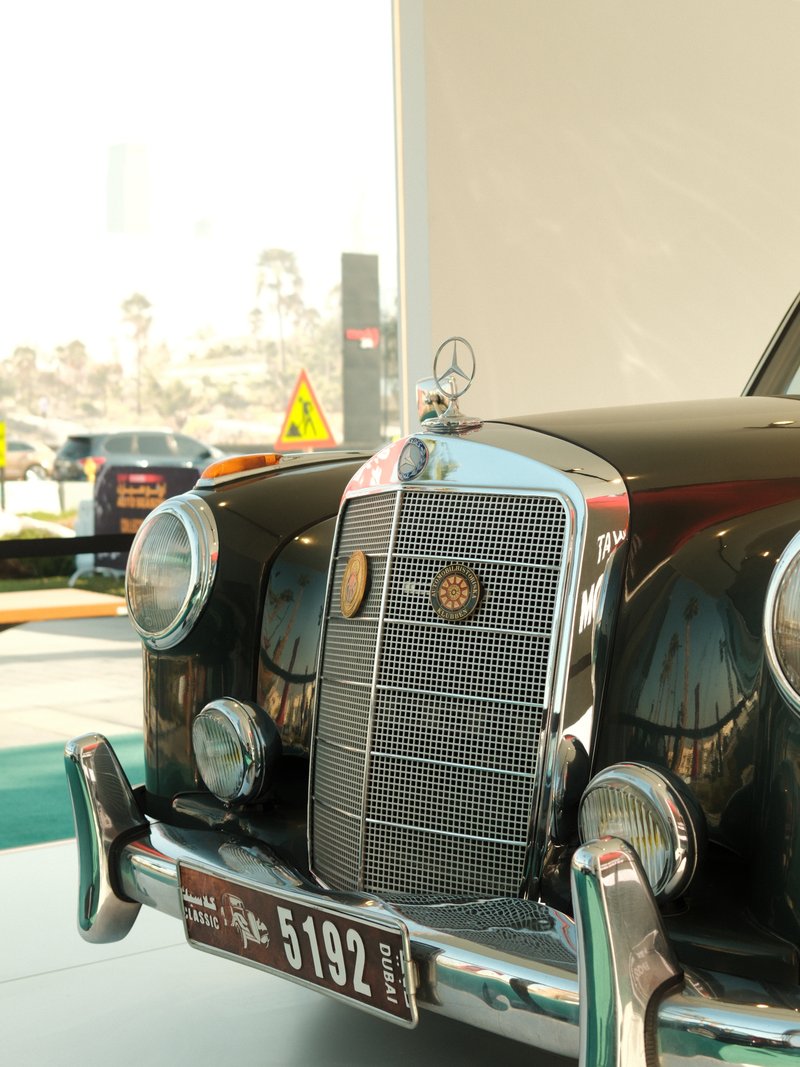 Close-up of a vintage black Mercedes-Benz car with a shiny grille and emblem in a bright indoor setting.