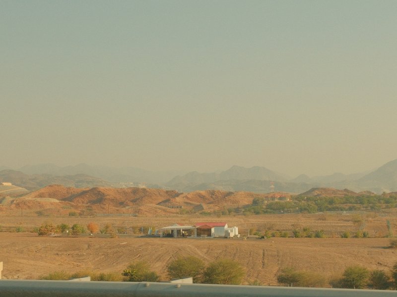 A distant view of a white building against a backdrop of dry, hilly terrain under a hazy sky.