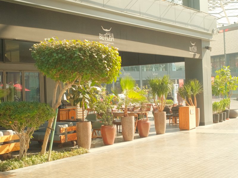 Outdoor restaurant patio with potted plants and seating under a shaded area.
