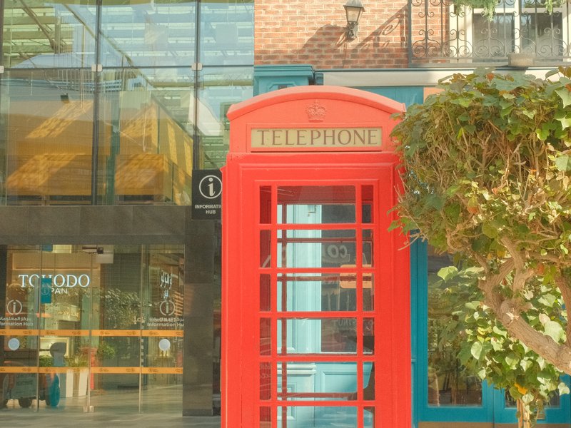A bright red telephone booth in front of a modern glass building.