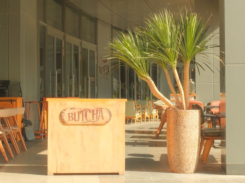 A wooden butcher sign next to a large potted palm plant outside a restaurant.