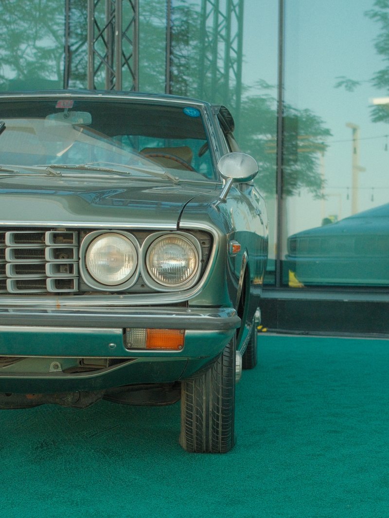 Close-up of a vintage car parked in front of a glass building with green carpet.