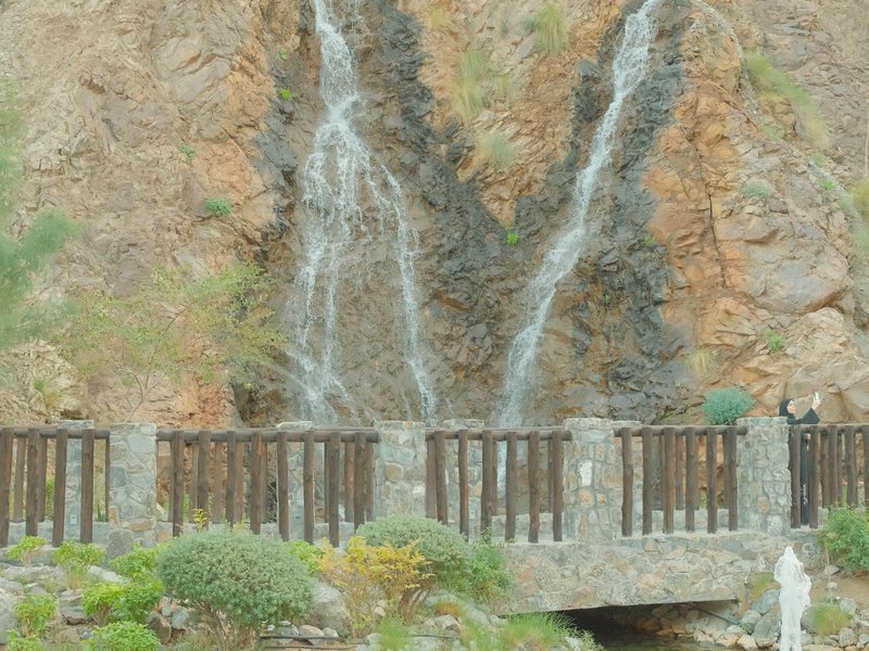 A scenic view of a waterfall cascading down rocky cliffs, with a stone bridge in the foreground.