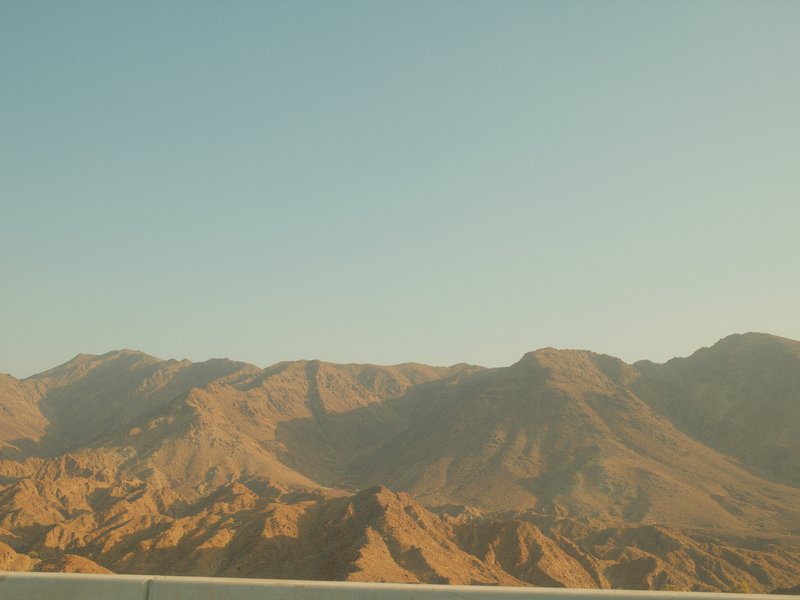A panoramic view of rugged mountains under a clear sky, showcasing earthy tones and textures.