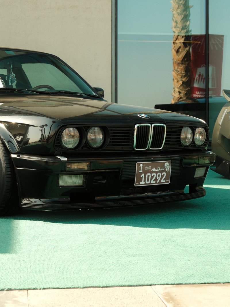A black BMW car parked on a green surface with a modern building in the background.