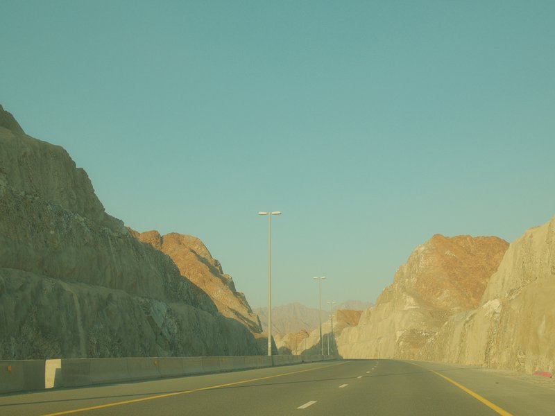 A scenic view of a highway flanked by rocky mountains under a clear blue sky.