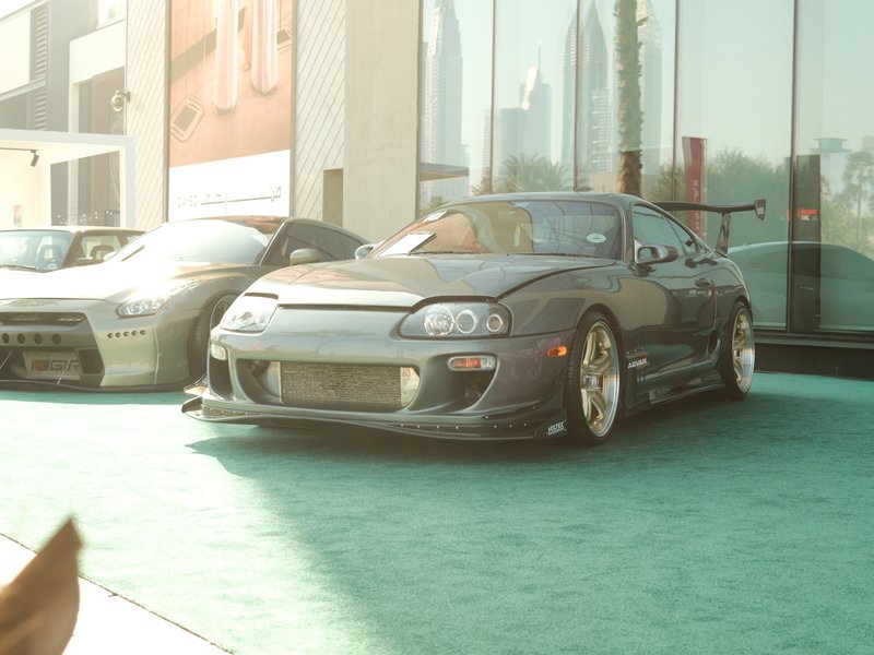 A modified sports car parked on a green surface with a modern building in the background.