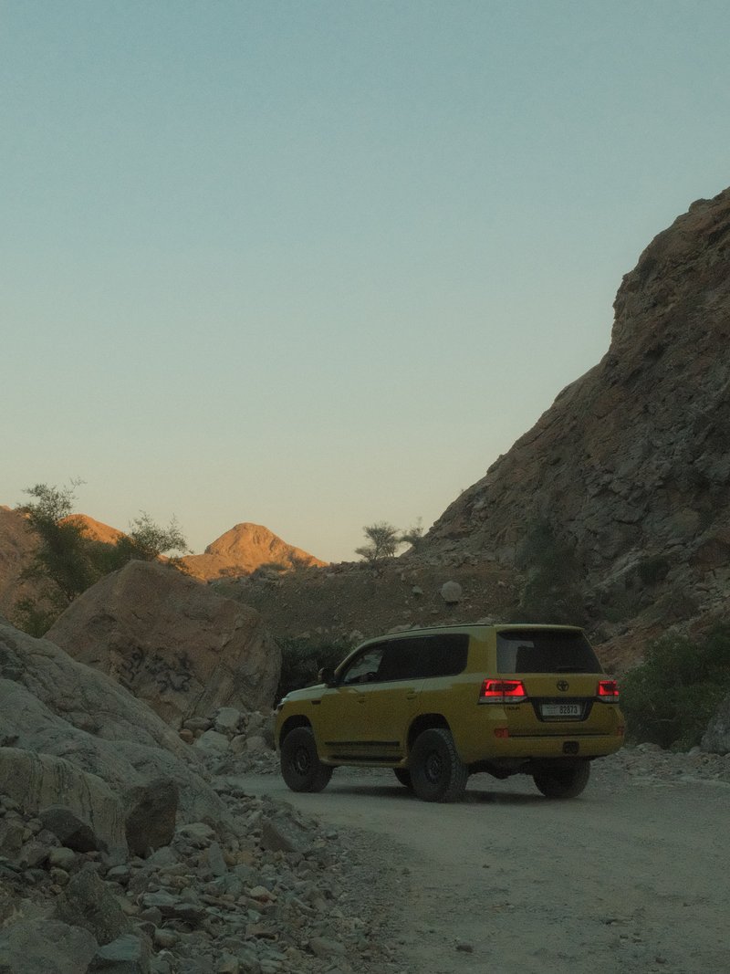 A yellow SUV navigating a rocky mountain road during twilight.
