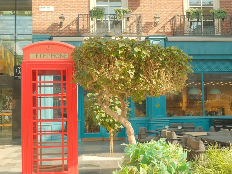 A red telephone booth beside a unique tree and a blue restaurant facade.