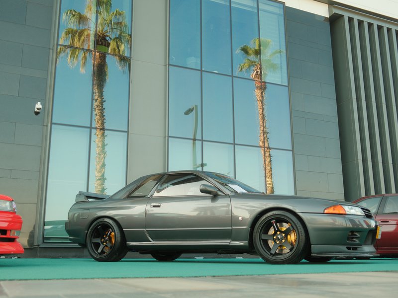A gray sports car parked beside a modern building with palm trees and reflective glass.