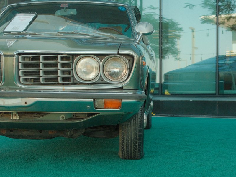 Close-up of a vintage car's front end with reflections in glass and a green carpet.