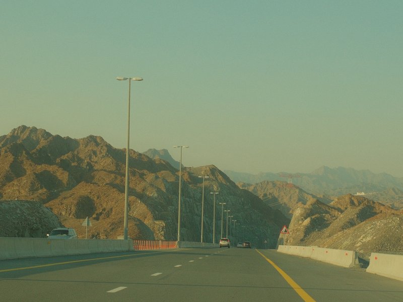A winding road through rocky mountains under a clear sky, with utility poles lining the roadside.