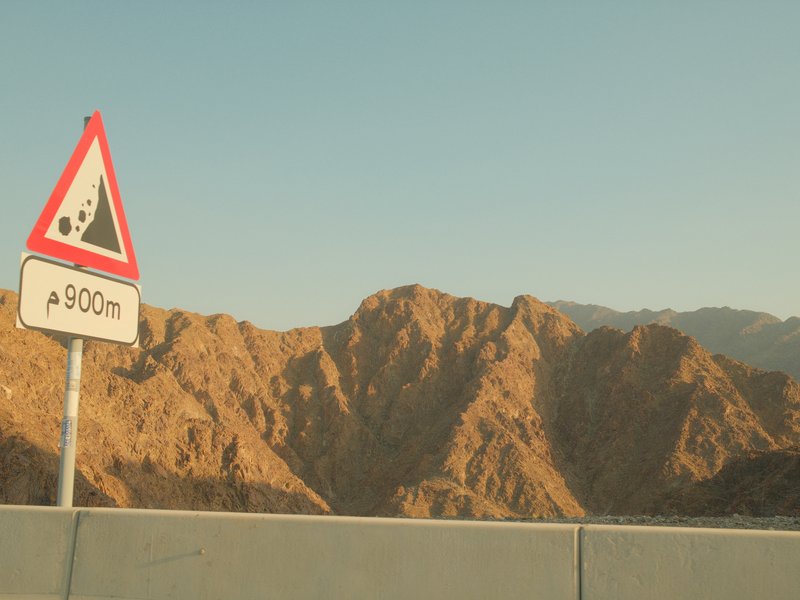 A warning sign indicating a steep descent, with rugged mountains in the background under a clear sky.