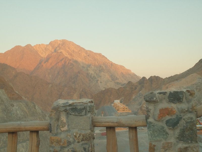 A rocky mountain range bathed in soft evening light, viewed from a stone wall.
