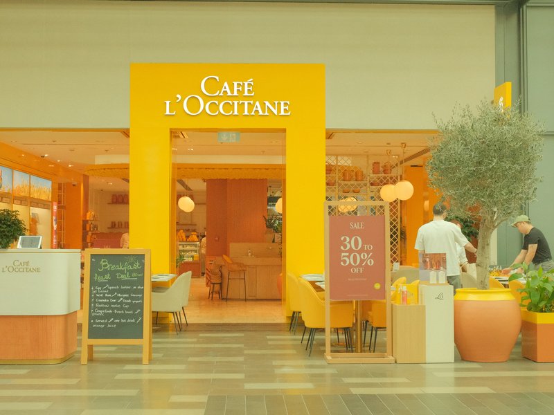 A bright café entrance with yellow accents, featuring a menu board and potted plants.