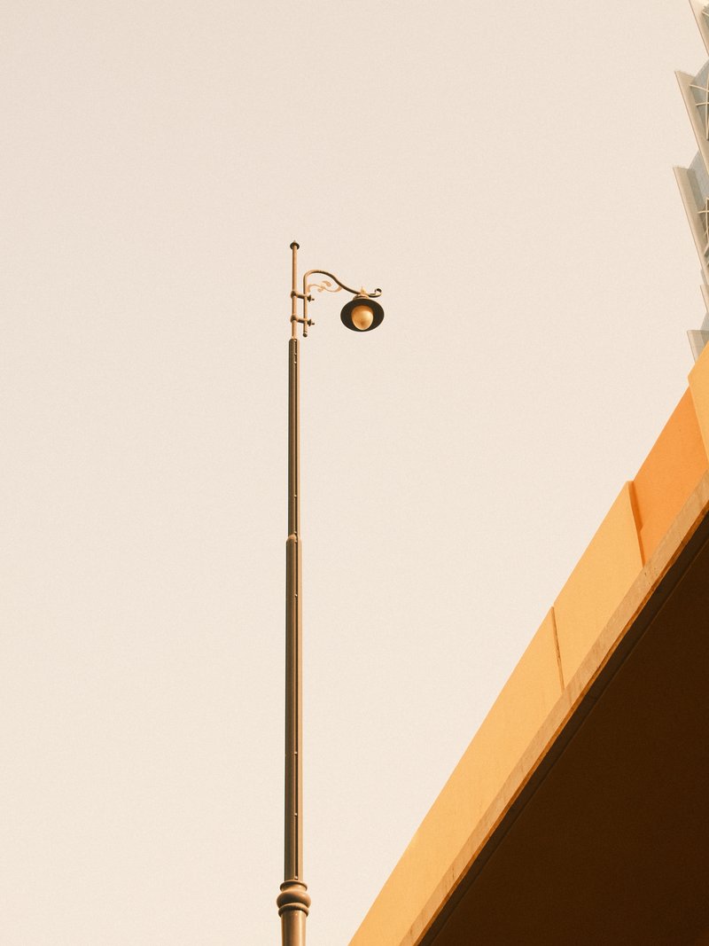 A tall street lamp against a pale sky, with a portion of a building visible in the corner.