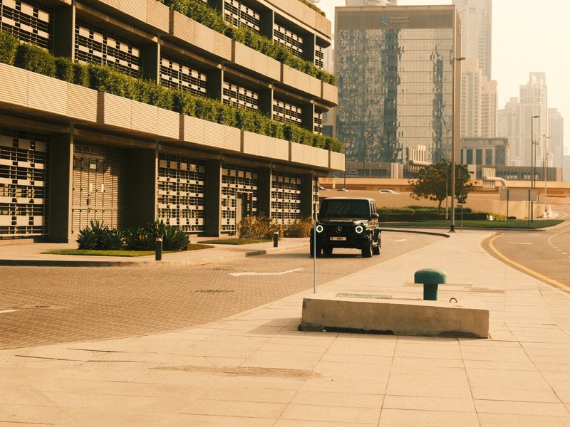 A modern urban street scene featuring a building with greenery and a parked black vehicle.