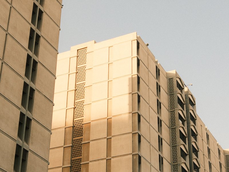 Modern concrete buildings with a warm light reflecting off their surfaces against a clear sky.