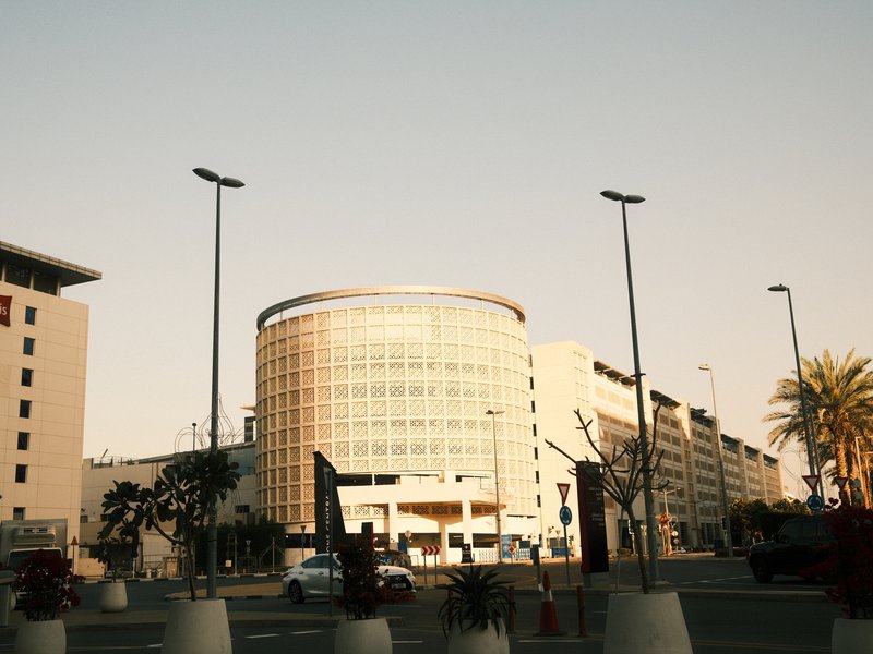 Modern buildings with glass facades under a clear sky, featuring palm trees and street lamps.
