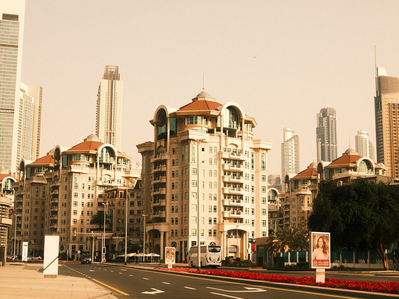A modern urban scene featuring tall buildings and a distinct architectural structure with a warm color tone.