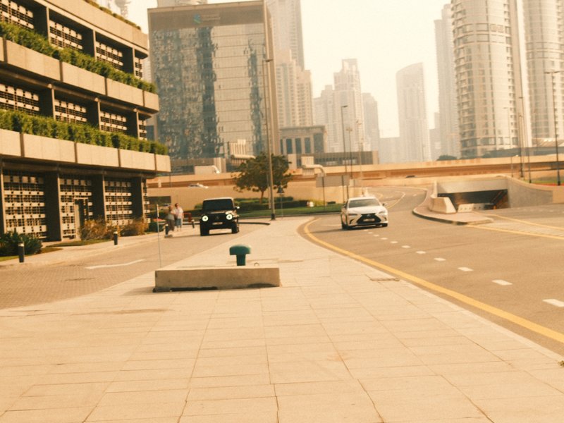 A wide urban street scene with modern buildings and vehicles under a hazy sky.